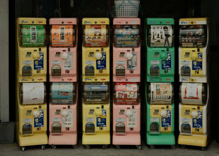 A row of multi-colored gacha machines in front of a shop in Japan.